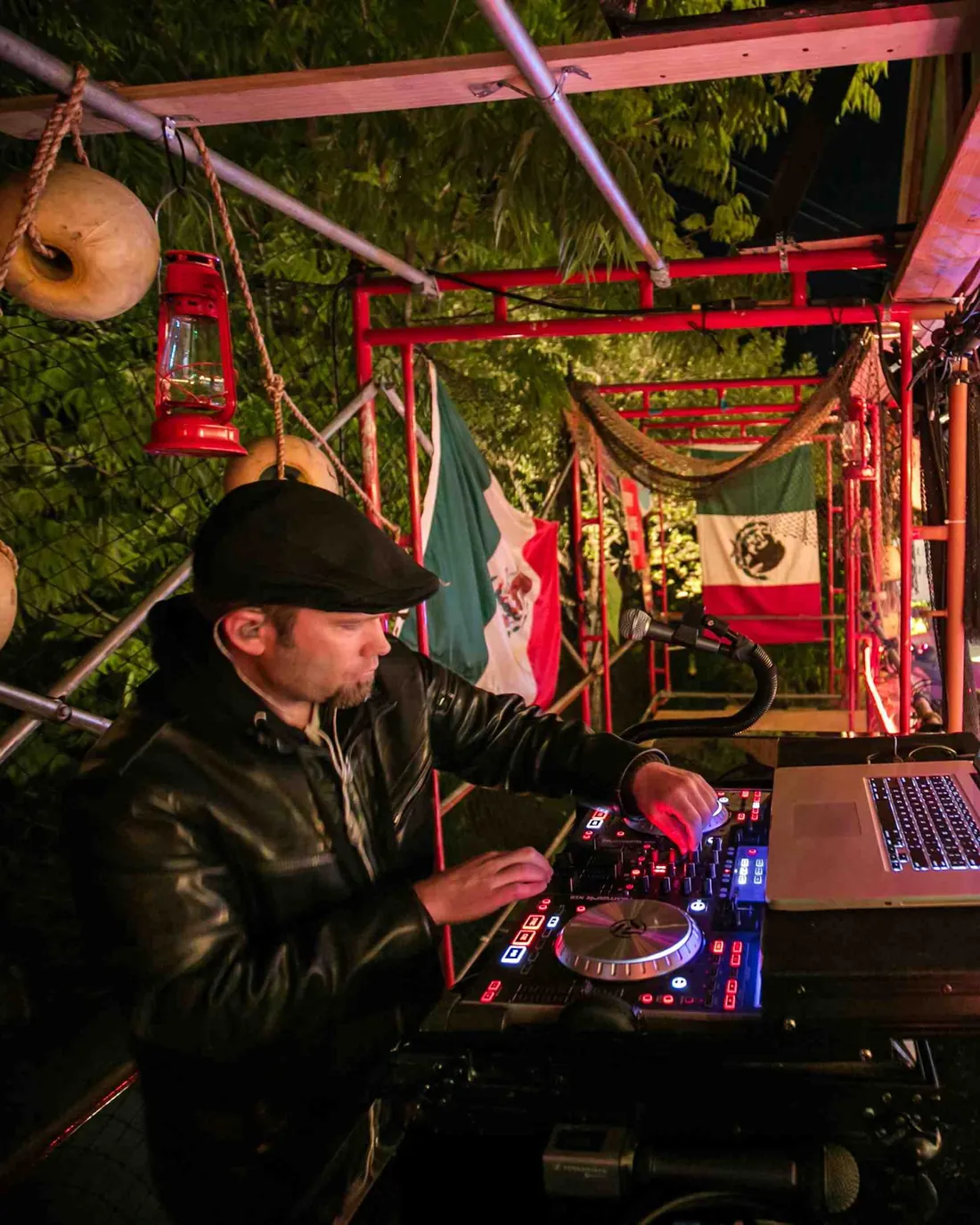DJ Wayne Noel, Bay Area event DJ and music director, mixing at night on the El Squido Row stage under red lights and flags