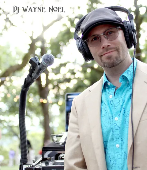 DJ Wayne Noel in headphones and a turquoise shirt at an outdoor set under the oak trees