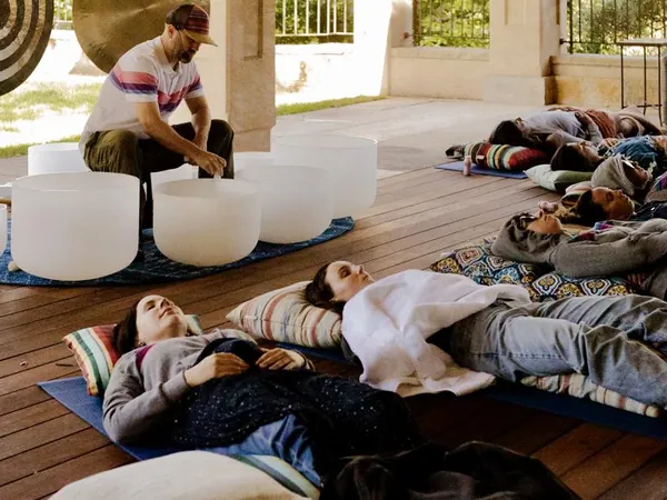 Guests lying on mats under blankets during a live sound bath while DJ Wayne Noel plays crystal singing bowls