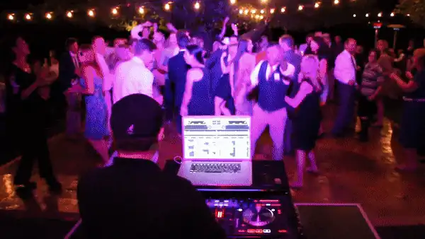 A packed outdoor wedding dance floor under string lights at Dawn Ranch in Guerneville, seen from DJ Wayne Noel's decks