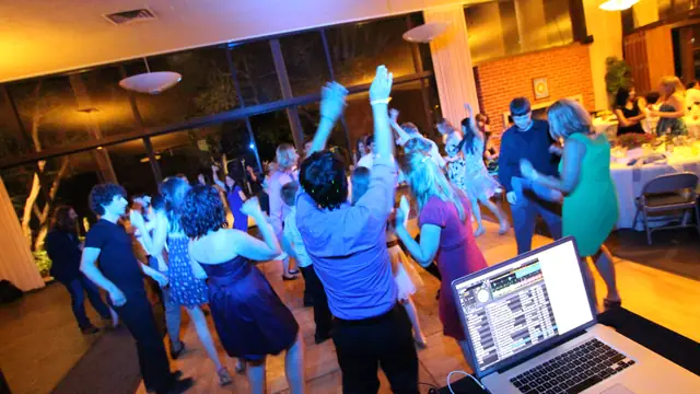 Dance floor at Alumni House, UC Berkeley seen from behind DJ Wayne Noel's laptop, guests dancing under blue and pink lighting by the window wall
