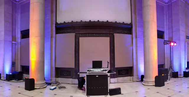 Wayne Noel's DJ booth and speakers set up before the bronze doorway in the grand hall at the Asian Art Museum in San Francisco, with columns lit in orange and blue