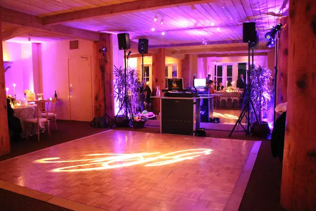 DJ booth and speakers set up beside a lit monogram dance floor in a timber-beamed room at Auberge du Soleil in Rutherford, uplit in purple