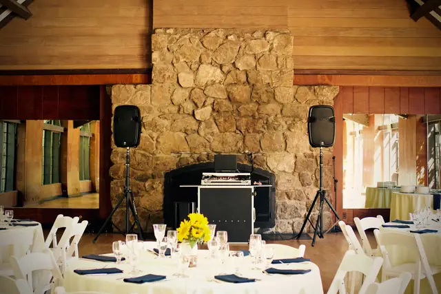 DJ booth and two speakers set in front of the stone fireplace in the Brazilian Room at Tilden Park, Berkeley, with tables set for a wedding