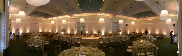 White-walled event room at Carneros Resort and Spa set for a wedding dinner, with warm white uplights at the foot of the walls and white pendant lamps overhead