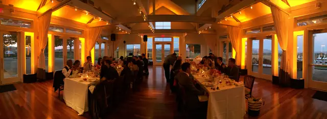 Amber-lit dinner reception at Carneros Resort and Spa with long tables under a vaulted beamed ceiling, a wood floor and glass doors along the walls