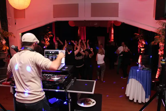 DJ rig set up on the wooden floor at Caspar Community Center with guests dancing with raised arms in the hall