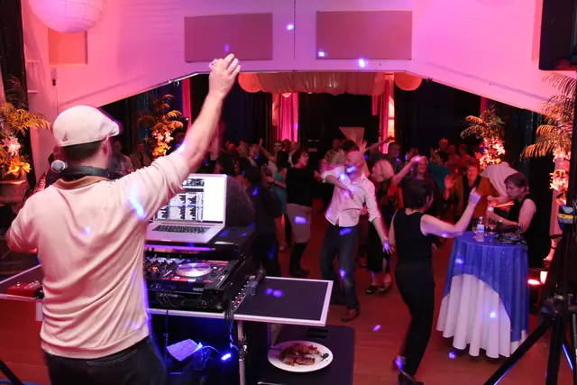 DJ Wayne Noel raises an arm behind the decks as guests fill the dance floor at Caspar Community Center in Caspar