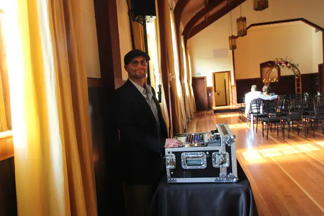 DJ Wayne Noel standing at his ceremony mixer beside the aisle in the timber-beamed hall at Cavallo Point