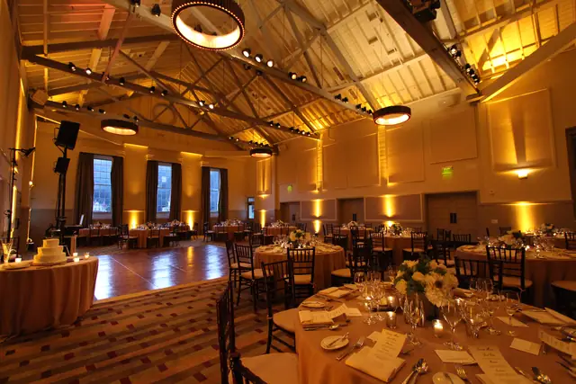 Parquet dance floor and cake table beside dinner tables in the amber-lit hall at Cavallo Point, with a DJ speaker stand at the left