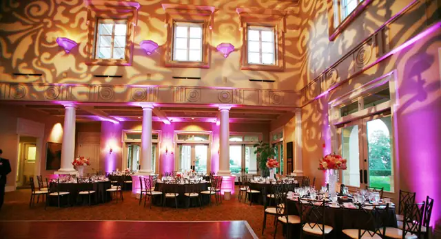 Ballroom at The Club at Ruby Hill set for dinner with pink uplighting on the columns and an amber pattern on the upper walls