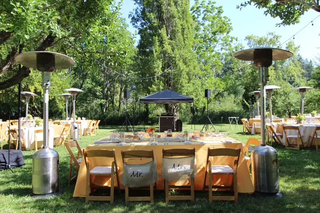 Apple orchard reception at Dawn Ranch in Guerneville with round tables, patio heaters and DJ Wayne Noel's canopy setup and speakers on the lawn