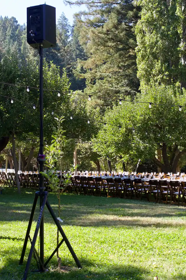 Speaker on a stand beside long banquet tables under string lights in the apple orchard at Dawn Ranch