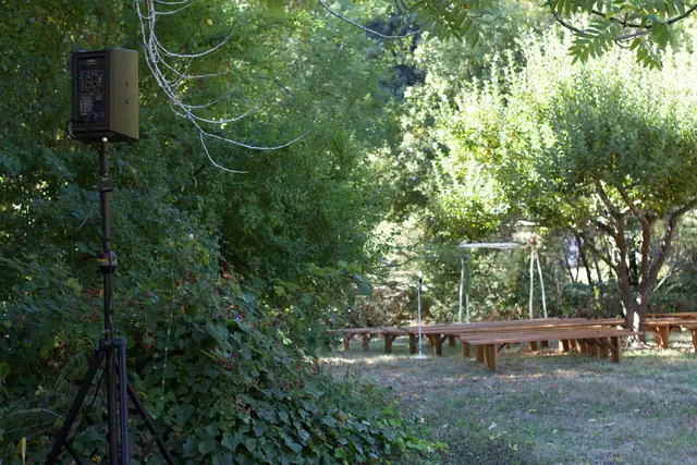 Wood benches and flower-topped arch for an outdoor ceremony at Dawn Ranch with a DJ speaker on a stand
