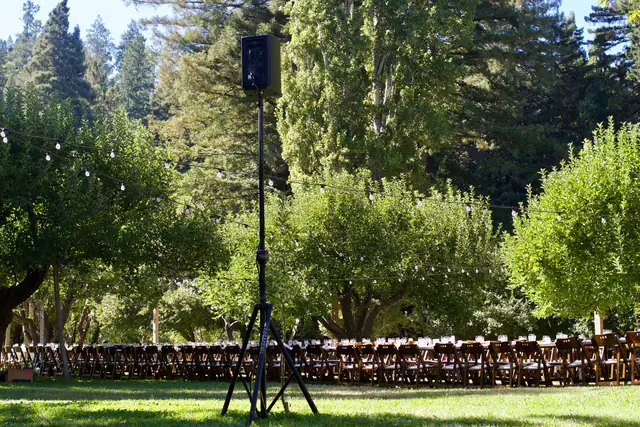 Long dinner tables set among apple trees and string lights at Dawn Ranch with a DJ speaker on a stand in front