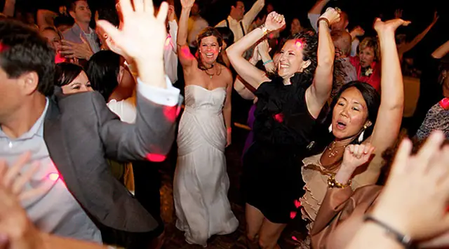 Bride and guests dancing with arms raised on a packed dance floor at Dawn Ranch in Guerneville