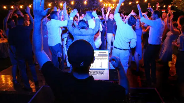 View over DJ Wayne Noel's shoulder at a packed outdoor dance floor under string lights at Dawn Ranch