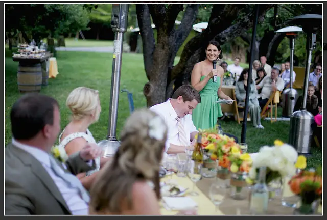 A bridesmaid giving a toast on a wireless microphone at an outdoor wedding dinner in the Apple Orchard at Dawn Ranch in Guerneville