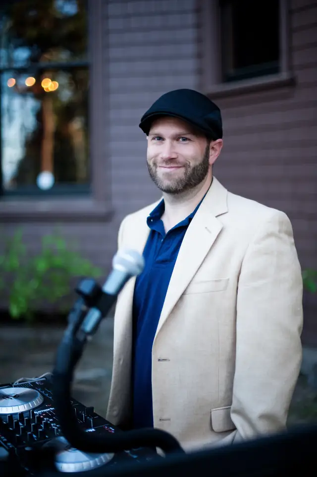 DJ Wayne Noel smiling behind his DJ controller and microphone against the brick wall of the Ehrman Mansion at Lake Tahoe