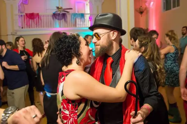 Guests dancing close on a full dance floor under the balcony of the Hotel Petaluma ballroom in Petaluma, lit in pink and teal