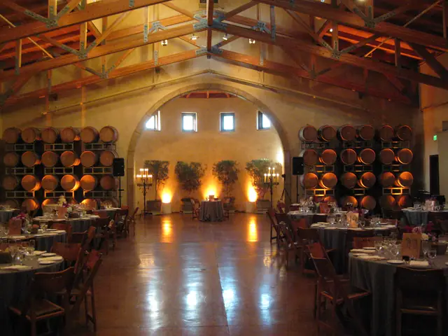 Barrel room at Jacuzzi Family Vineyards in Sonoma, set for a wedding dinner under timber trusses with stacked wine barrels lit in amber and a stone arch at the far end