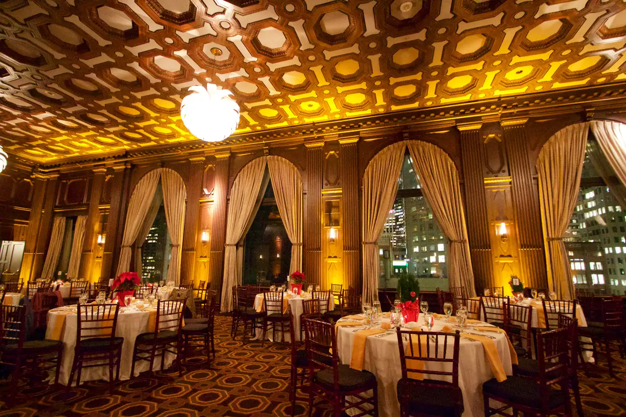 Julia Morgan Ballroom in San Francisco set for a dinner, with a coffered wood ceiling, arched windows with gold drapes and round tables