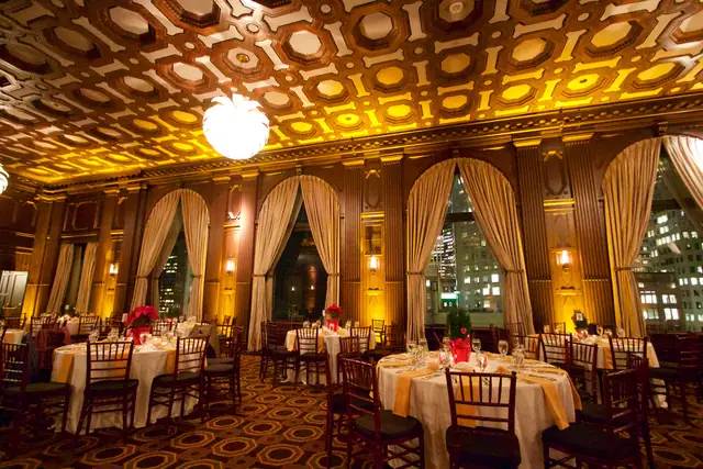 Julia Morgan Ballroom in San Francisco set for a dinner, with a coffered wood ceiling, arched windows with gold drapes and round tables