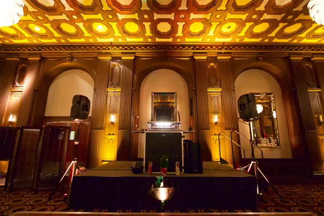 DJ booth and speakers on a stage riser in front of a paneled arch at the Julia Morgan Ballroom in San Francisco