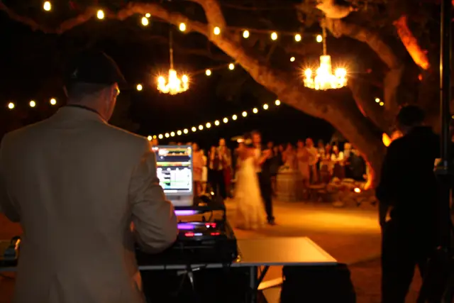 DJ Wayne Noel at the decks during a first dance under chandeliers and string lights in the oak grove at Kunde Family Winery