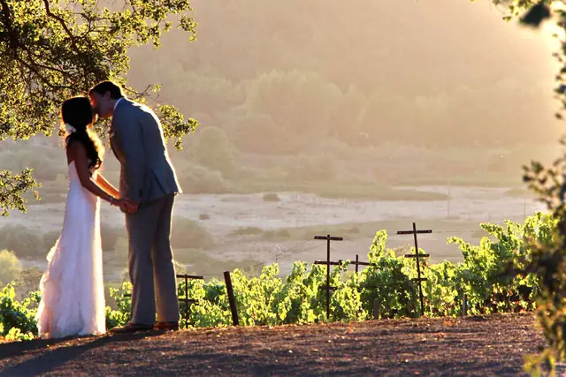 A bride and groom kiss beside the vineyard rows at sunset on Boot Hill at Kunde Family Winery in Kenwood