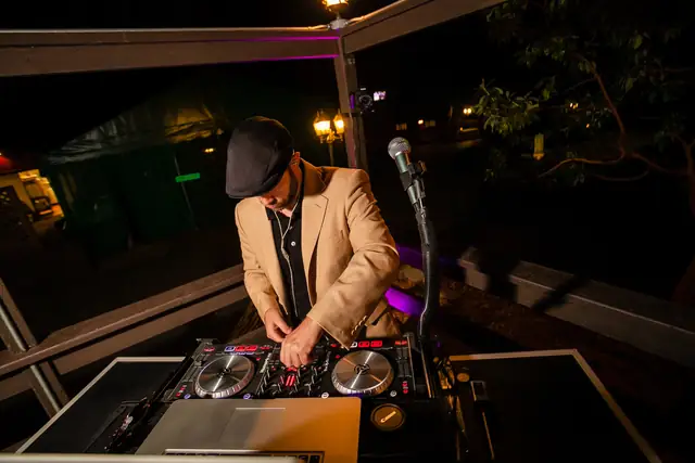 DJ Wayne Noel mixing on a controller under the wooden deck beams at Little Hills in San Ramon at night