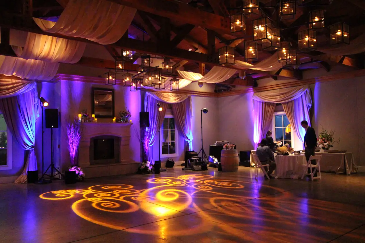 Stone Room at The Lodge at Sonoma with timber beams, lantern chandeliers, fireplace, purple uplighting and amber swirl lighting on the floor