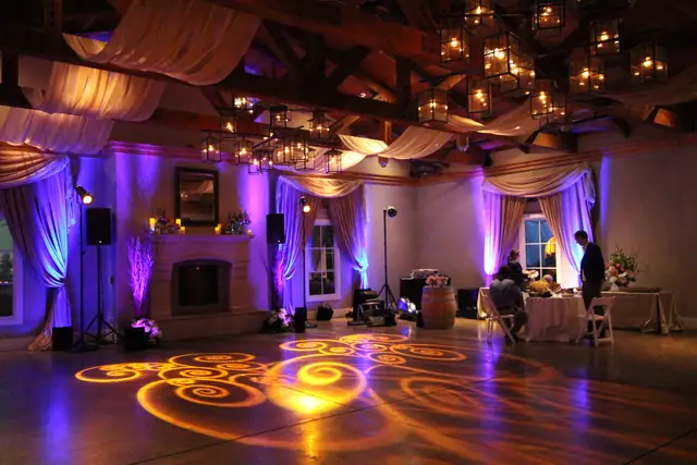 Stone Room at The Lodge at Sonoma with timber beams, lantern chandeliers, fireplace, purple uplighting and amber swirl lighting on the floor