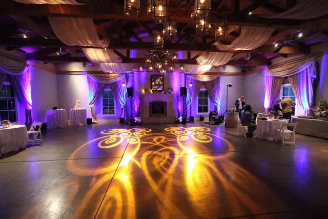 Beamed ballroom at The Lodge at Sonoma with lantern chandeliers, lavender uplighting and a gold gobo pattern on the dance floor