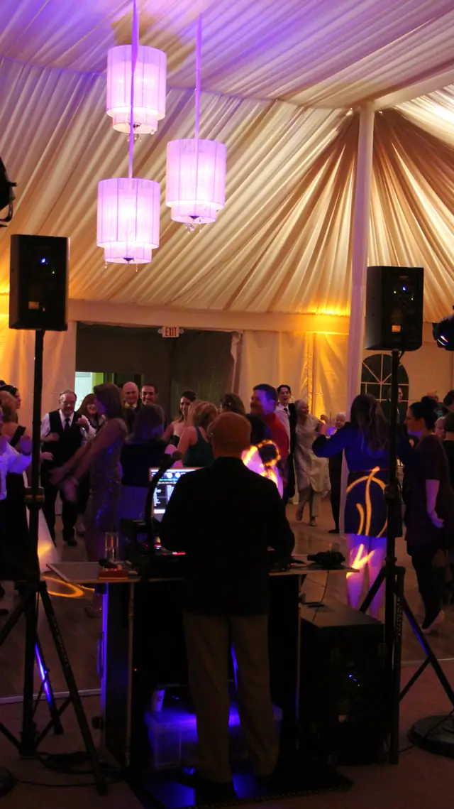 Wayne Noel DJing from behind his booth while guests dance under purple-lit chandeliers at The Lodge at Sonoma