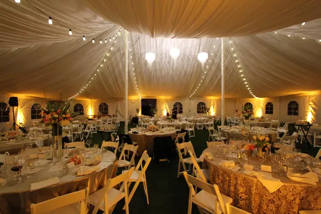 Reception tent at The Lodge at Sonoma set for dinner with string lights, chandeliers and amber uplighting