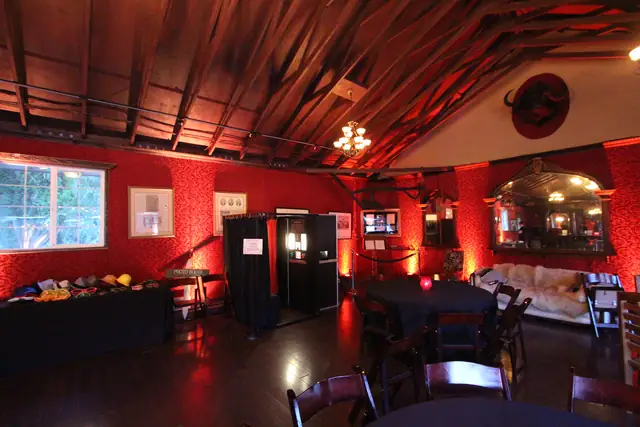 Long Branch Saloon in Half Moon Bay set for a reception, with red uplighting on the wallpapered walls, timber rafters, a photo booth and round tables