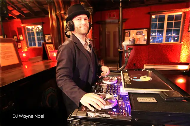 DJ Wayne Noel in a bowler hat at the decks inside the red-walled Long Branch Saloon in Half Moon Bay, a candlelit bar behind him