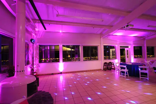 Pink-lit dance floor beside a white column and round fireplace at Mavericks House