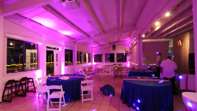 Long reception room at Mavericks House with pink uplighting along the walls and ceiling, round tables set at the far end