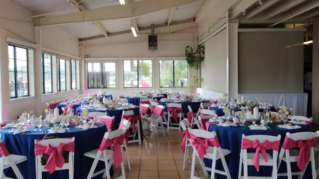 Reception tables set with navy linens, glassware and pink chair sashes at Mavericks House, with a pull-down screen behind