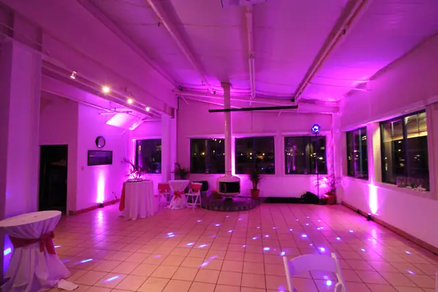 Open tile dance floor lit with pink uplighting and blue points of light at Mavericks House, with a white fireplace and cocktail tables