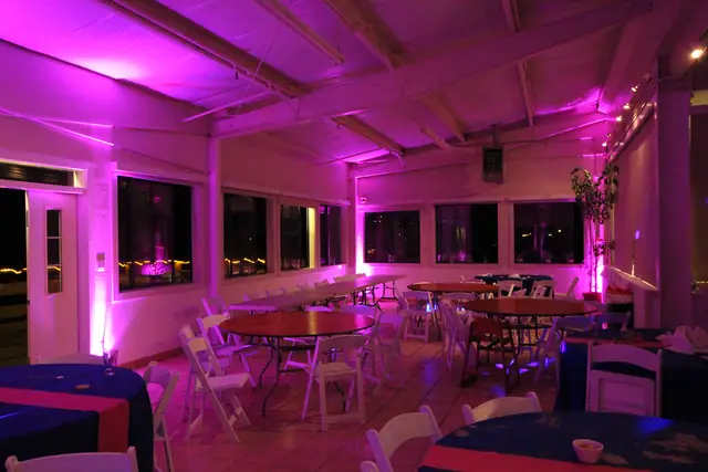 Pink-lit seating area with round tables and windows at Mavericks House
