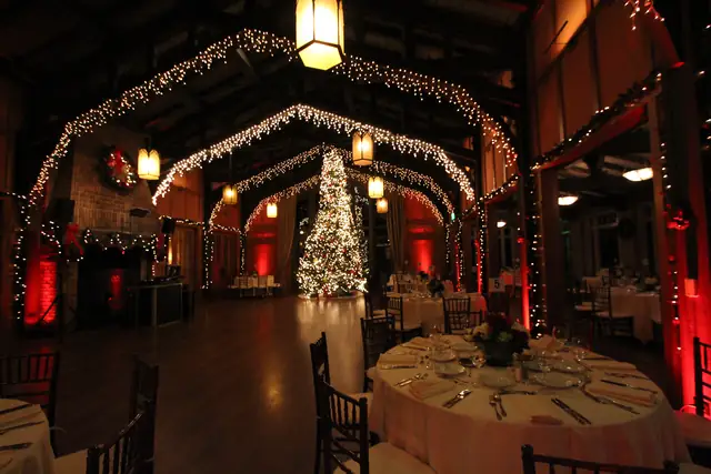 Looking down the Meadow Club hall through lit wooden arches toward a tall tree, with the DJ booth by the fireplace at left