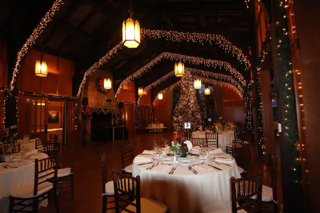 Meadow Club hall with arched trusses, hanging lanterns and a set round table, DJ setup visible at the far fireplace