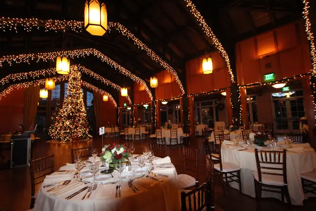 Set dinner table in the foreground of the Meadow Club hall with lit arches, a tall tree and French doors beyond