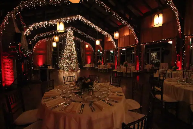 Dim Meadow Club hall with red uplit brick pillar, lit arches and a tall tree, tables set for dinner