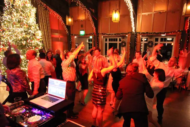 Guests dancing with their arms raised in front of the DJ booth and Christmas tree at the Meadow Club in Fairfax