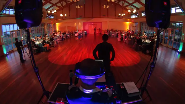DJ Wayne Noel at the decks facing the wood dance floor and seated guests at the Mill Valley Community Center