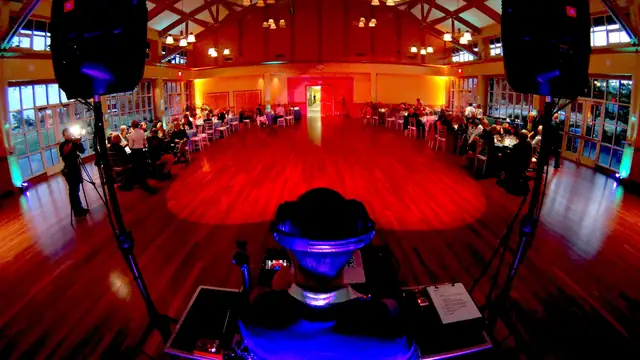 View from behind the DJ at Mill Valley Community Center, looking across the hardwood floor to seated dinner guests and the windowed hall
